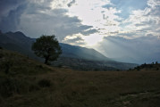 einzelner Baum, Sonne zwischen dicken Wolken und Lunxhërisë-Gebirgszug